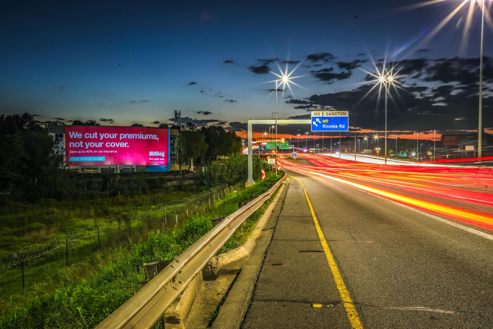 Illuminated MiWay billboard printed on PVC alongside a highway at dusk
