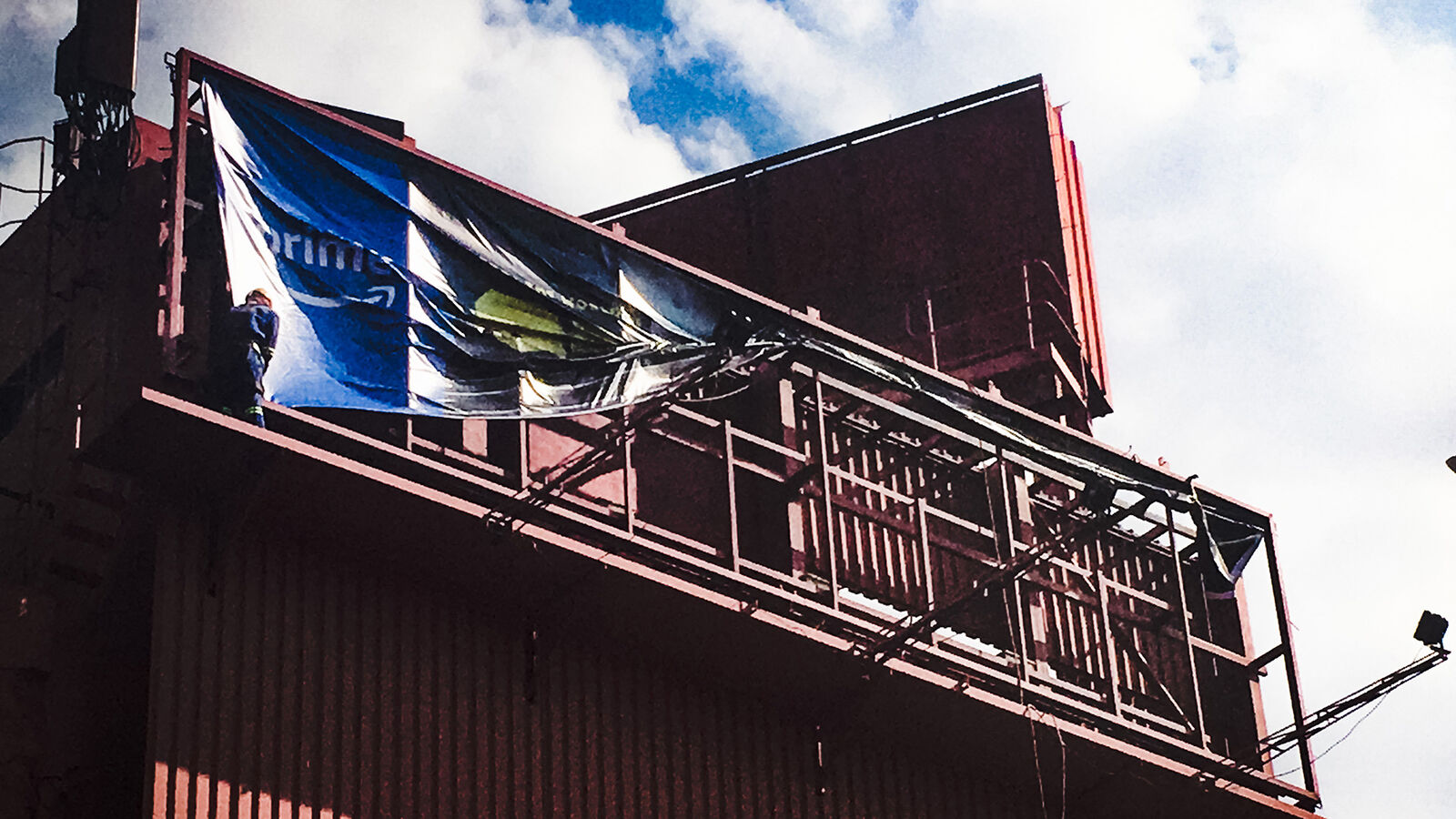 Crew installing a large printed Amazon Prime banner on a rooftop billboard frame